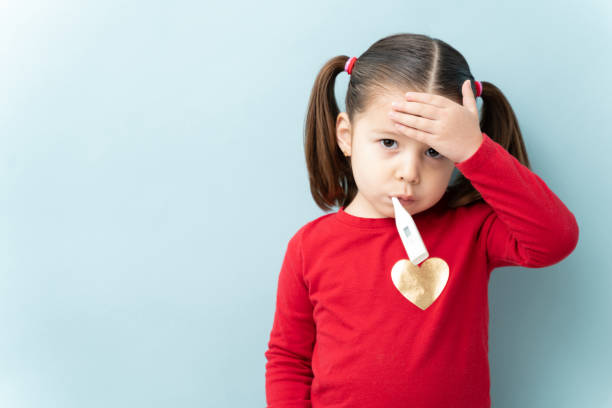 Little girl with fever touching her forehead Pretty little girl with ponytails touching her forehead and using a thermometer to check for a fever in a studio fever stock pictures, royalty-free photos & images