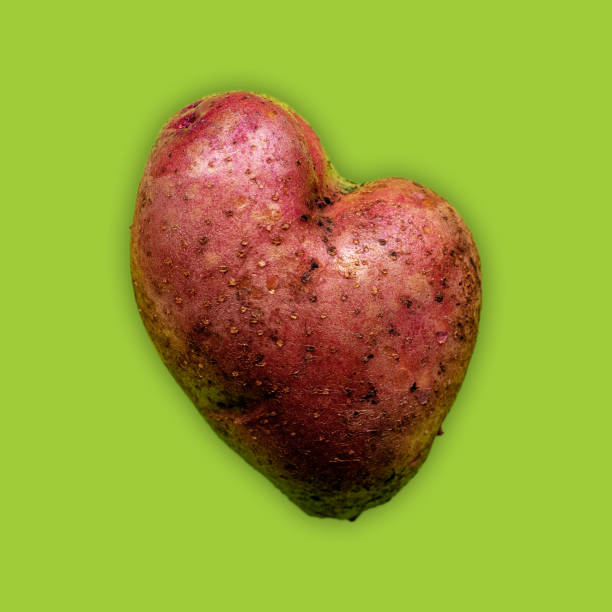 緑色の背景に赤い皮が付いたハート型のジャガイモ - heart shape raw potato food individuality ストックフォトと画像