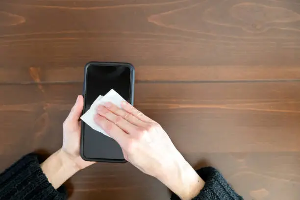 Photo of Woman cleaning display of smart phone with antibacterial white tissue or disposable wipes