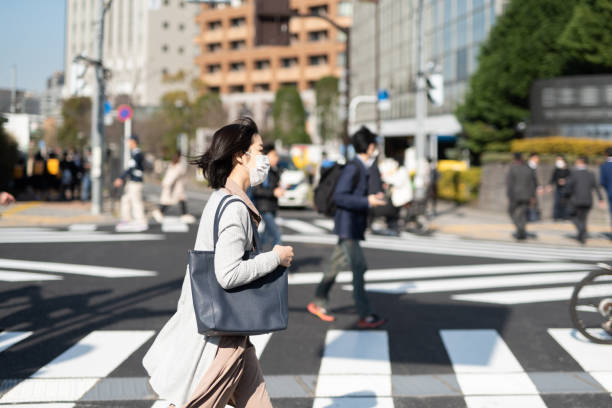 femme d’affaires avec le masque chirurgical marchant dans la ville - japan tokyo prefecture city women photos et images de collection