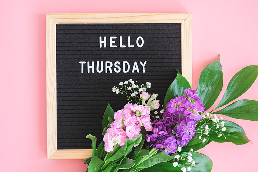 Hello Thursday text on black letter board and bouquet colorful flowers on pink background. Concept Happy Thursday. Template for postcard, greeting card Flat lay Top view.