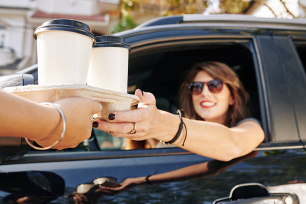 Waiter giving coffee cups to female driver Waiter giving disposable tray with two cups of take out coffee to pretty smiling female driver drive through photos stock pictures, royalty-free photos & images