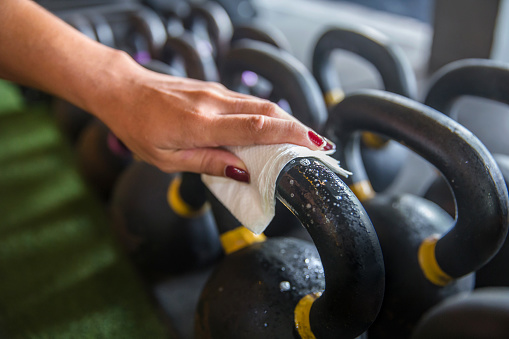 Close up shot female hands cleaning kettlebell before workout to kill bacteria & virus