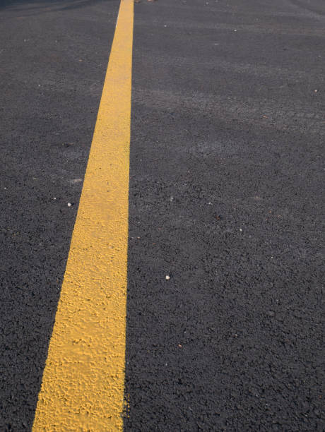 istock Yellow line across dark asphalt 1214172278