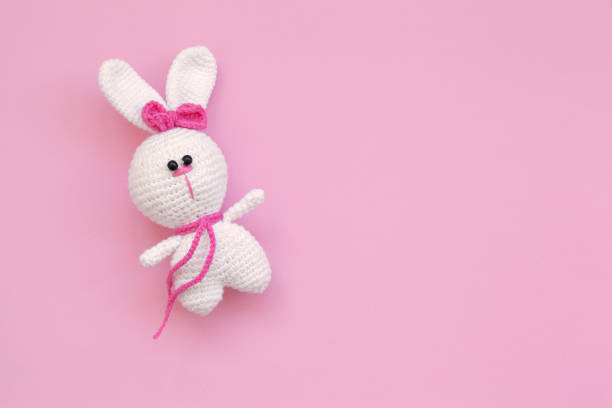 A small knitted baby toy-rabbit on pink background. Flat lay, top view. stock photo