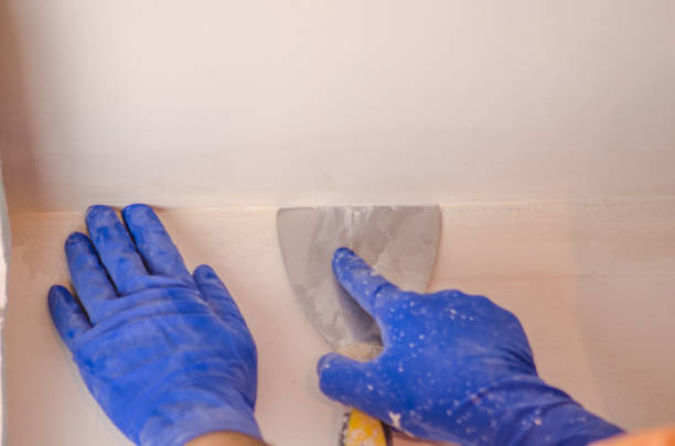 istock The Builder puts plaster on the wall.Hand holding a spatula with construction mix and smoothes out bumps.Repair the wall.Plaster the wall with a putty knife. 1214189679