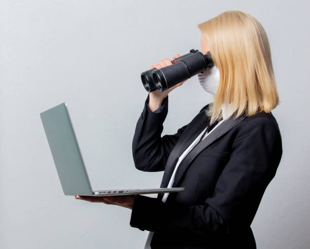 istock Businesswoman in black suit and face mask with binoculars and computer 1214205401