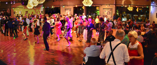 Workshop classes. Indoor line dancing by a professional instructor. Herent, Belgium - September 14, 2019: Open House indoor dancing classes evening show. Photo reportage open door promotion indoor dance classes. Courses starting half September. Teacher (not in view)in front of large group demonstrates solo dance. Selective focus blurred dancers. Elderly couple, man suspenders, lady red dress having a talk. Other sitting around a table drinking a beer. teacher retirement party stock pictures, royalty-free photos & images