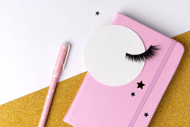 Creative composition with notepad and eyelashes on pink golden glitter background