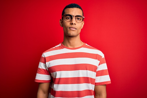 Young handsome african american man wearing casual striped t-shirt and glasses Relaxed with serious expression on face. Simple and natural looking at the camera.