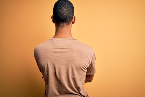 Young handsome african american man wearing casual t-shirt standing over yellow background standing backwards looking away with crossed arms