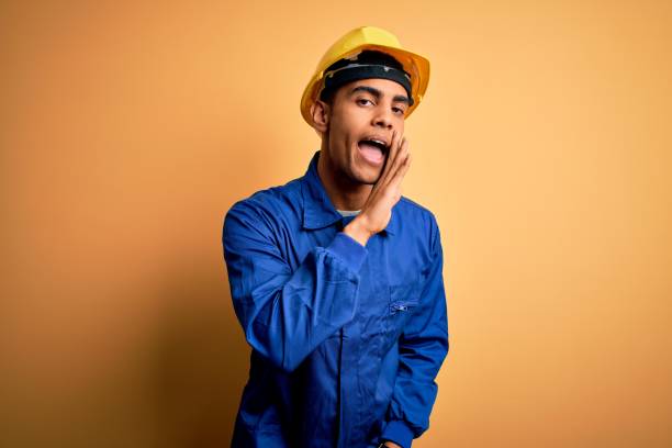 istock Young handsome african american worker man wearing blue uniform and security helmet hand on mouth telling secret rumor, whispering malicious talk conversation 1214211835