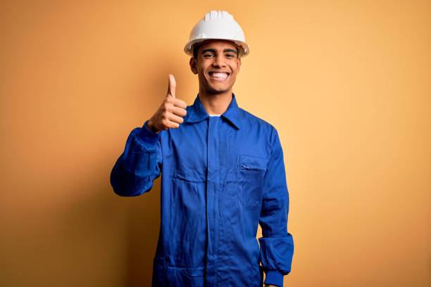 istock Young handsome african american worker man wearing blue uniform and security helmet doing happy thumbs up gesture with hand. Approving expression looking at the camera showing success. 1214212021