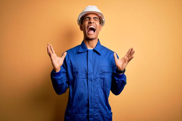 istock Young handsome african american worker man wearing blue uniform and security helmet celebrating mad and crazy for success with arms raised and closed eyes screaming excited. Winner concept 1214212030