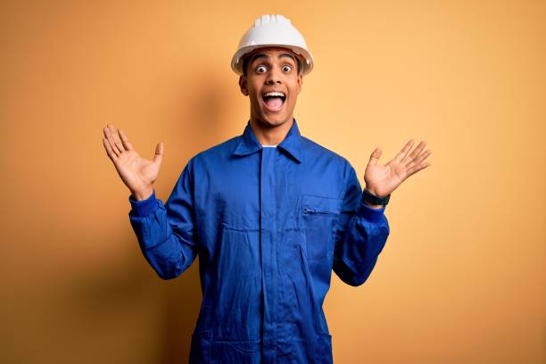 istock Young handsome african american worker man wearing blue uniform and security helmet celebrating crazy and amazed for success with arms raised and open eyes screaming excited. Winner concept 1214212041