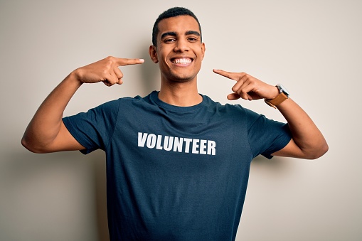 Young handsome african american man volunteering wearing t-shirt with volunteer message smiling cheerful showing and pointing with fingers teeth and mouth. Dental health concept.