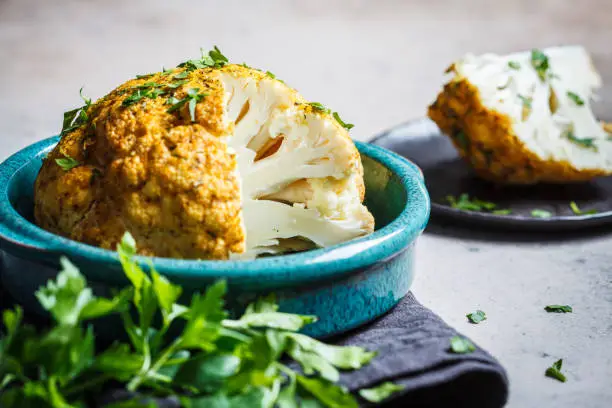 Whole baked cauliflower with spices and herbs. Healthy vegetarian food concept.