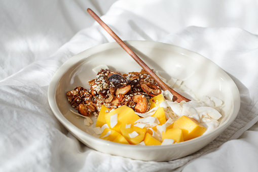 Breakfast in bed - homemade granola, yogurt and mango in a bowl.