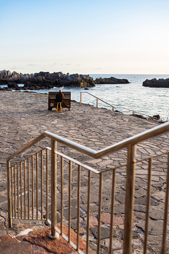 An elderly man playing a piano in a harbour, in front of the Atlantic ocean at a beautiful sunset.