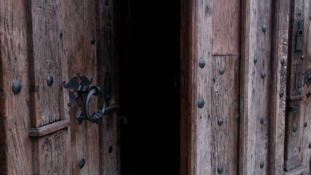 Close-up of closing old wooden door with metal handle in ancient medieval Catholic church.