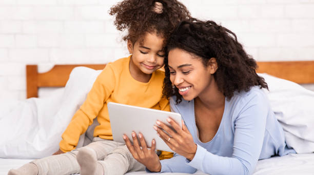 istock African Mother And Daughter Using Digital Tablet Lying In Bed 1214220445
