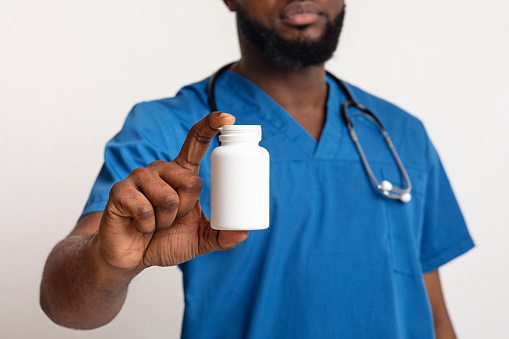 Cropped view of african american male doctor in blue uniform with pill bottle on white studio background