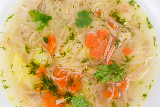 Fragment of white dish with homemade chicken soup with thin short vermicelli close-up, top view, background