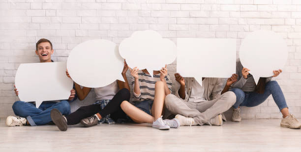 istock Happy guy sitting among friends covering faces with speech bubbles 1214222267