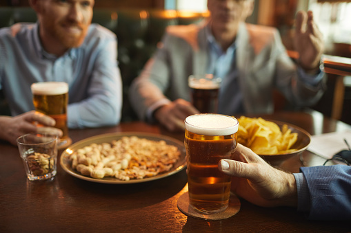 Close-up of young men drinking beer with snacks and talking to each other while sitting at the table in the pub