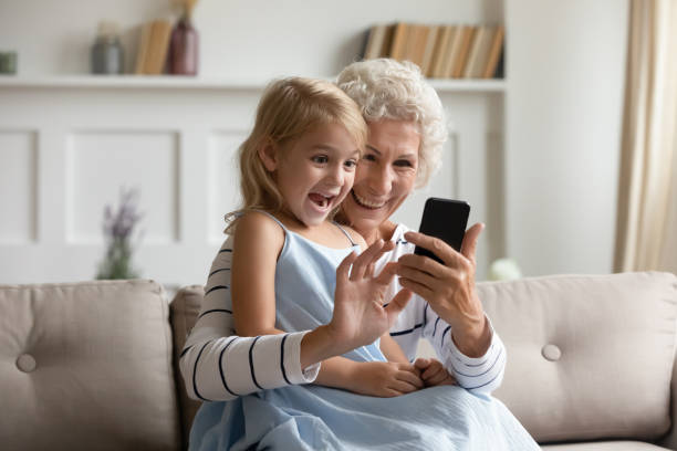 istock Smiling little girl using smartphone with senior granny 1214223576