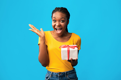 Gifts And Presents. Happy African Woman Holding Wrapped Box Shouting In Excitement Posing On Blue Studio Background.