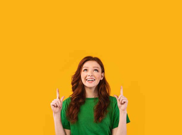 istock Cheerful Red-Haired Girl Pointing Fingers Up At Copyspace, Studio Shot 1214226118