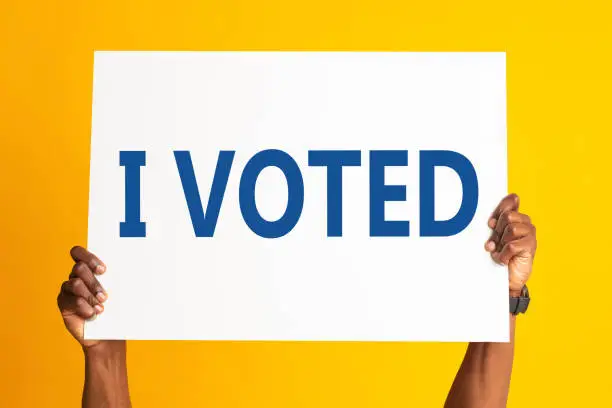 Photo of African American patriot holding sign with inscription I VOTED on color background, close up