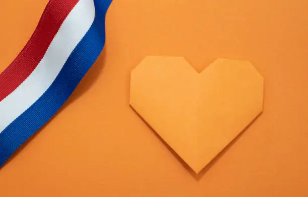 An orange paper heart on an orange background with a ribbon in red white and blue. Room for copy.