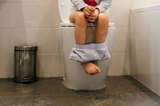 Using The Toilet Close up of young Caucasian girls legs sat on the toilet in the bathroom with her pyjama pants round her ankles. potty toilet child bathroom stock pictures, royalty-free photos & images