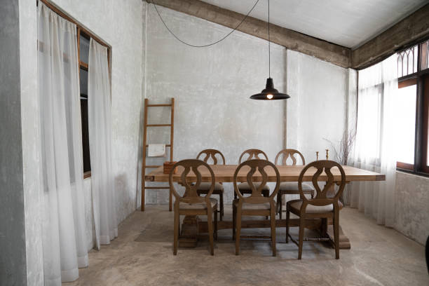istock Stylish modern loft dining area with natural light scene and bare concrete wall with natural wood table and chairs setting  / interior design 1214230899