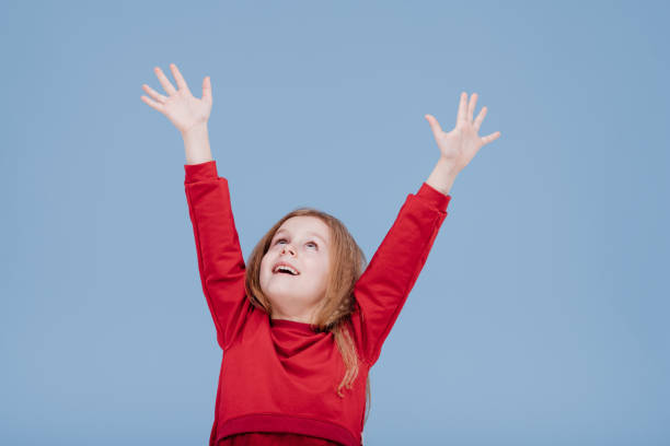 little girl with her hands up, dressed in red, isolated on blue background, in studio