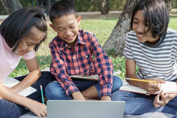 istock Group of Asian elementary school children working together and information search learning with laptop in the summer at the park. The schoolgirl came to study field trip and activity learned outdoor 1214235323