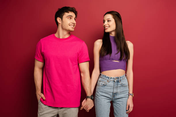 istock smiling young couple holding hands and looking at each other on red 1214239397
