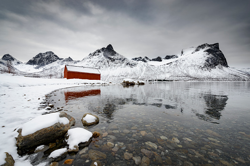 Panoramic view on the island Senja island in Northern Norway during a cold winter day. The grounds and mountains are covered in snow under a dark stormy sky.