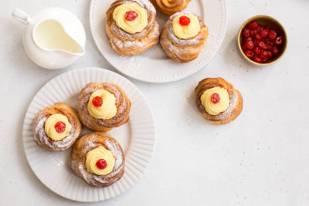 zeppole of St. Joseph Italian pastry - zeppole di San Giuseppe - baked cream puffs made from choux pastry, filled and decorated with custard cream and cherry. It is eaten to celebrate Saint Joseph's Day. choux pastry photos stock pictures, royalty-free photos & images