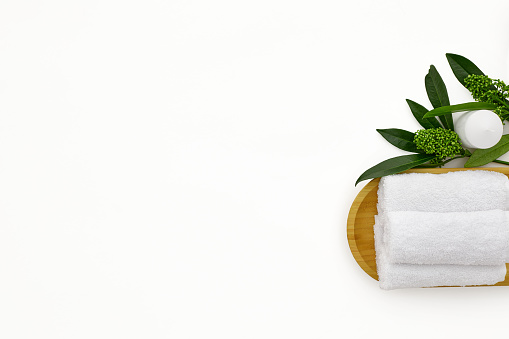 wellness and spa composition with towels, candle and tropical leaves on white background. top view. copy space
