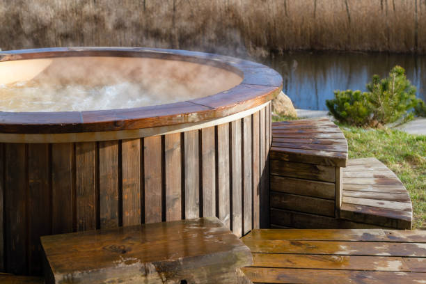 comment l’eau tourbillonnant dans le bain à remous en bois à l’extérieur dans la nature. bénéficiant d’une piscine à vapeur chaude par une journée ensoleillée, un traitement privé au spa. personne - bâtiment vu de lextérieur photos et images de collection