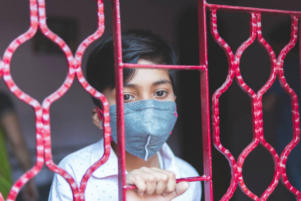 der traurige junge schützt sich und trägt eine maske gegen das corona-virus - curfew stock-fotos und bilder