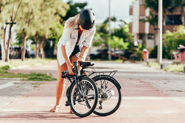 mujer joven preparando su bicicleta plegable al aire libre - plegar fotografías e imágenes de stock
