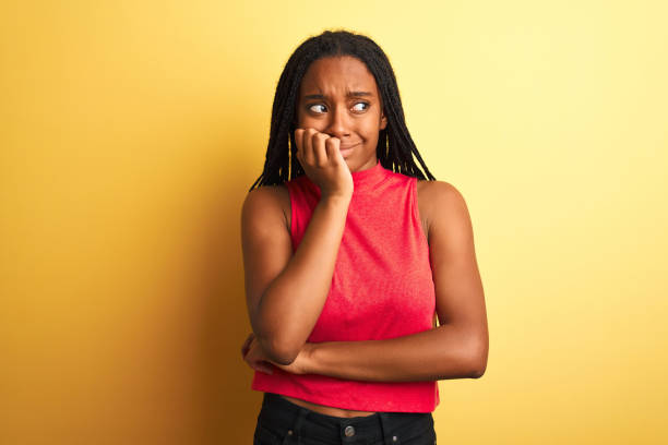 African american woman wearing red casual t-shirt standing over isolated yellow background looking stressed and nervous with hands on mouth biting nails. Anxiety problem. African american woman wearing red casual t-shirt standing over isolated yellow background looking stressed and nervous with hands on mouth biting nails. Anxiety problem. nail biting stock pictures, royalty-free photos & images