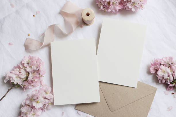istock Wedding stationery mock-up scene. Blank greeting cards, envelope on linen tablecloth background with pink blossoming cherry tree branches and ribbon. Feminine still life composition. Flat lay,top view 1214253663
