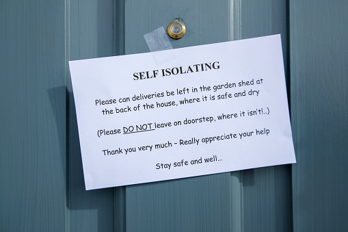 A printed paper sign taped to someones blue painted front door, alerting delivery drivers that the household is self isolating during the Coronavirus epidemic. The printed texts asks for deliveries to be left in a garden shed, rather than ringing the doorbell wanting an in person drop off.
