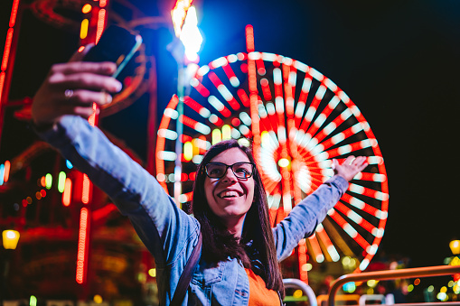 Cheerful young Caucasian woman enjoying time in amusement park. Making selfie for ma memory.
