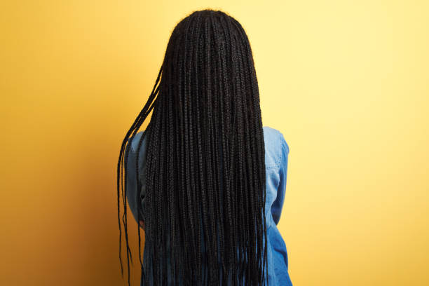 joven mujer afroamericana con camisa de mezclilla de pie sobre el fondo amarillo aislado de pie hacia atrás mirando hacia otro lado con los brazos cruzados - trenzas fotografías e imágenes de stock